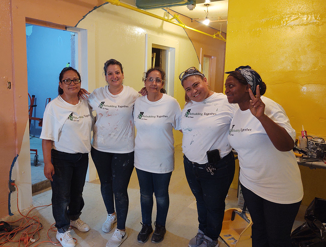 Five women standing side by side in Rebuilding Together El Paso shirts in a hallway of the project site.